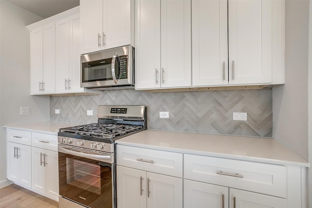 kitchen with appliances with stainless steel finishes, light hardwood / wood-style flooring, white cabinetry, and backsplash