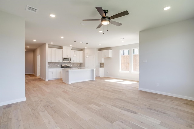 kitchen with an island with sink, white cabinetry, stainless steel appliances, pendant lighting, and light hardwood / wood-style flooring