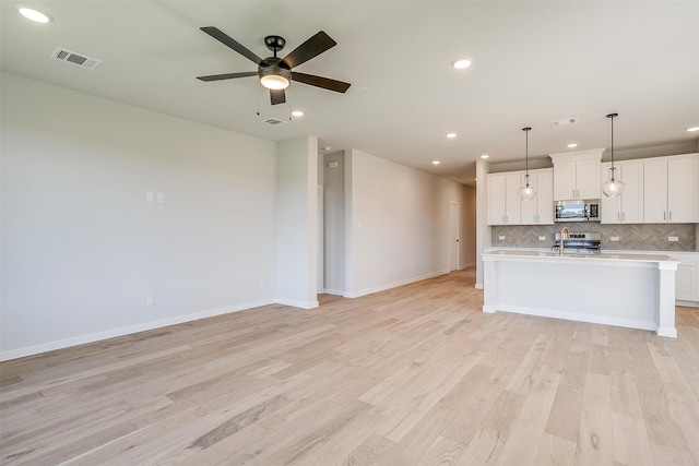 kitchen featuring appliances with stainless steel finishes, light hardwood / wood-style flooring, white cabinets, and hanging light fixtures