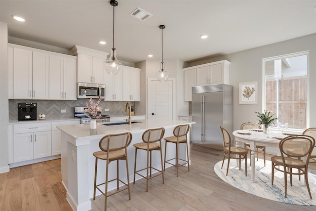 kitchen with sink, appliances with stainless steel finishes, light hardwood / wood-style flooring, and an island with sink