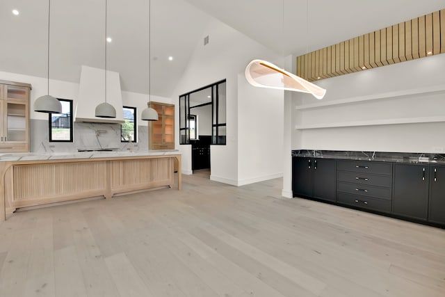 kitchen featuring light wood-type flooring, hanging light fixtures, tasteful backsplash, and high vaulted ceiling