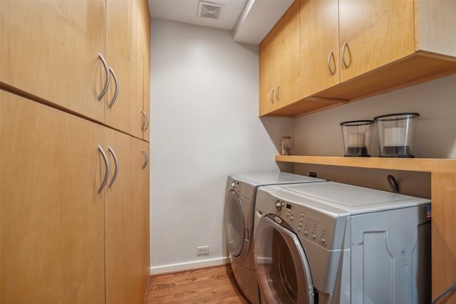 clothes washing area featuring cabinets, separate washer and dryer, and light wood-type flooring