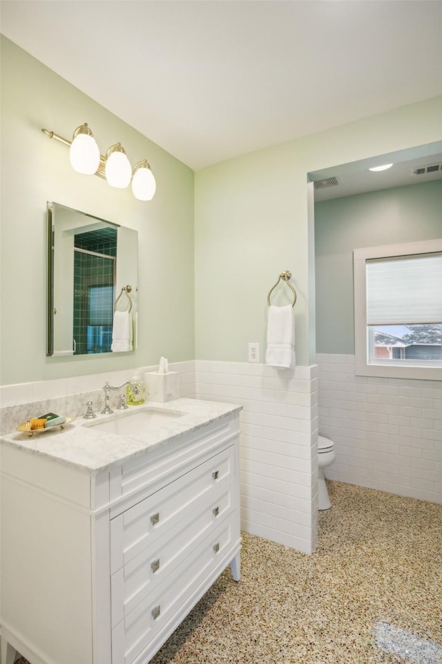 5332 Edmondson Ave, Dallas, TX 75209 - full bathroom featuring tile walls, vanity, toilet, wainscoting, and speckle patterned floor
