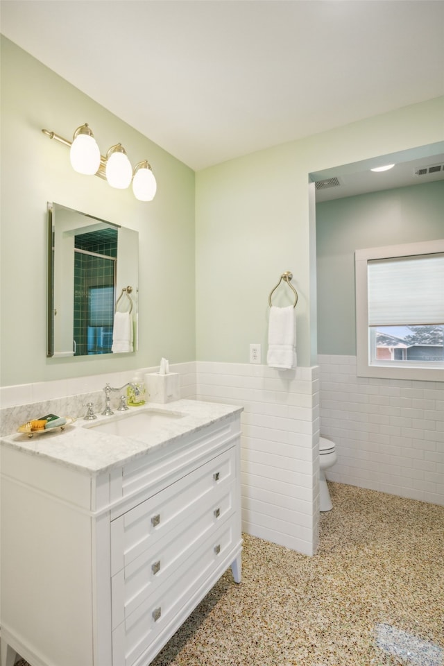 bathroom with vanity, toilet, and tile walls