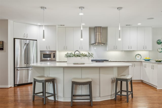 kitchen featuring a center island, hardwood / wood-style flooring, stainless steel appliances, and wall chimney exhaust hood