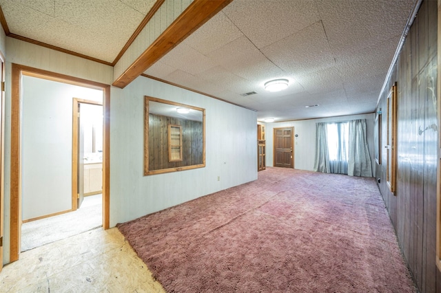 empty room with carpet, ornamental molding, and wooden walls