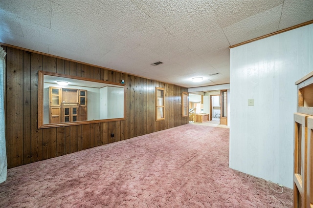 carpeted empty room featuring a textured ceiling and wood walls