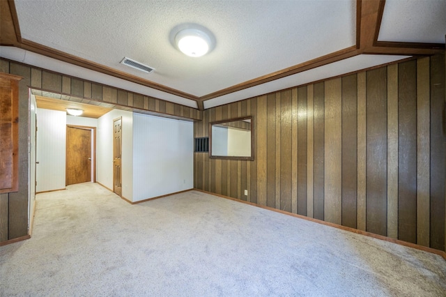 spare room featuring carpet, wooden walls, and a textured ceiling