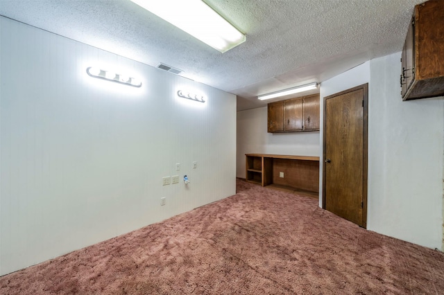 basement featuring a textured ceiling, built in desk, and light colored carpet