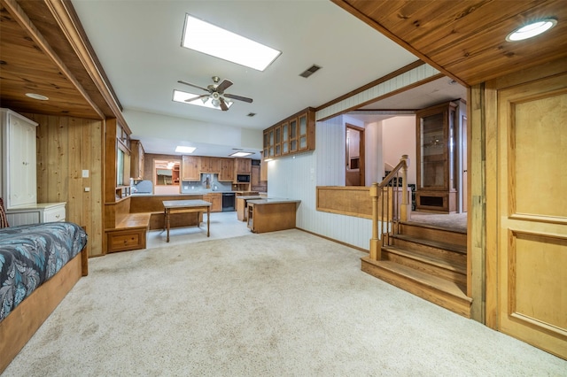 kitchen featuring kitchen peninsula, light colored carpet, ceiling fan, a skylight, and wooden walls