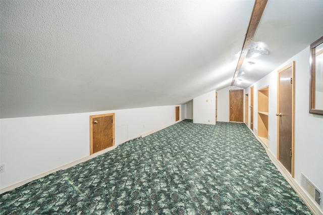 additional living space featuring dark carpet, vaulted ceiling, and a textured ceiling