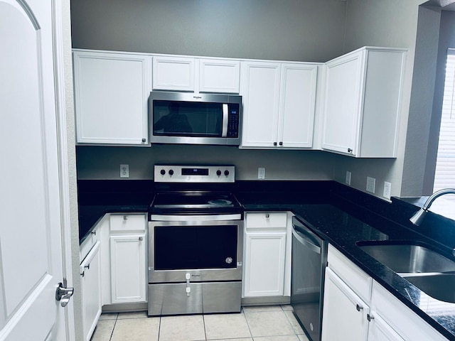 kitchen featuring dark stone countertops, white cabinetry, stainless steel appliances, and light tile patterned floors