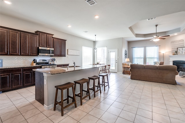 kitchen with stainless steel appliances, decorative backsplash, a kitchen bar, a center island with sink, and a raised ceiling