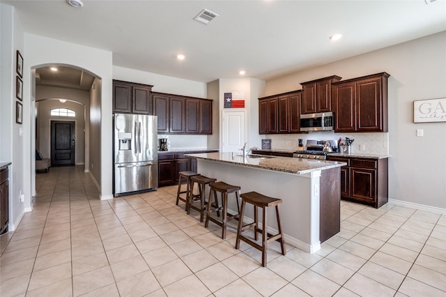 kitchen with sink, a kitchen bar, a kitchen island with sink, stainless steel appliances, and light stone countertops