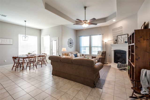 living room with light tile patterned flooring, ceiling fan, and a tray ceiling