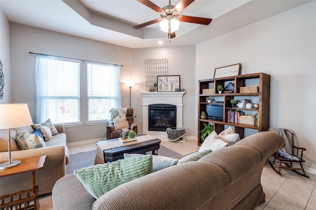 living room with a raised ceiling, light tile patterned floors, and ceiling fan