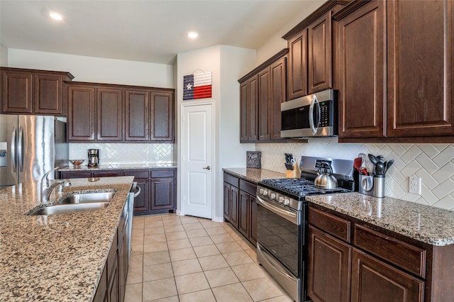 kitchen featuring sink, light tile patterned floors, appliances with stainless steel finishes, light stone counters, and dark brown cabinetry