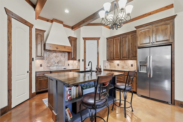 kitchen with a center island with sink, stainless steel fridge, custom range hood, and an inviting chandelier