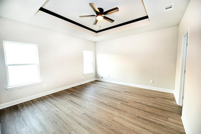 empty room featuring ceiling fan, a tray ceiling, and light wood-type flooring