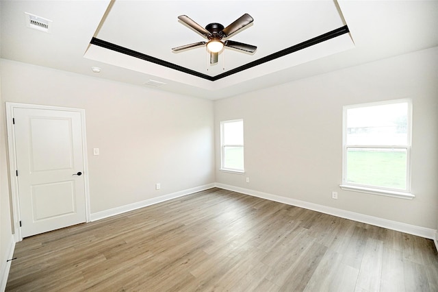 unfurnished room with a raised ceiling, ceiling fan, and light wood-type flooring