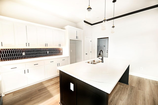 kitchen featuring a center island with sink, sink, hanging light fixtures, light hardwood / wood-style flooring, and white cabinetry