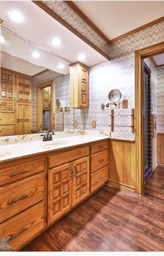 bathroom featuring wallpapered walls, ornamental molding, a sink, and wood finished floors