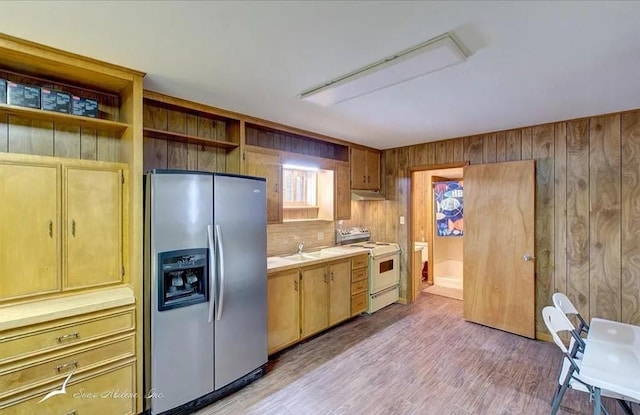 kitchen with wood walls, white range, stainless steel refrigerator with ice dispenser, light countertops, and under cabinet range hood