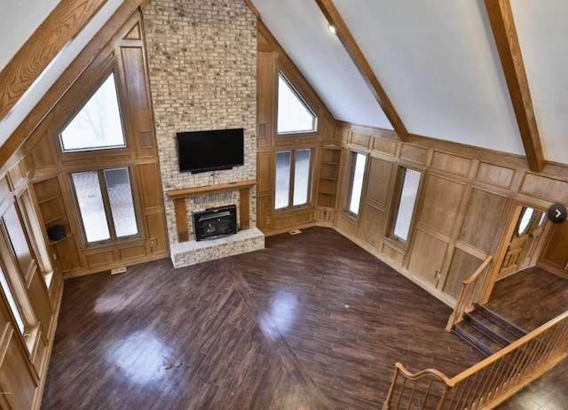 unfurnished living room featuring dark wood-style flooring, a decorative wall, a fireplace, high vaulted ceiling, and beamed ceiling