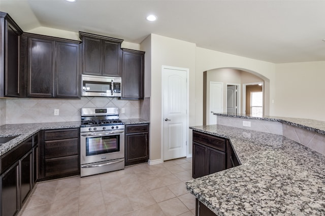 kitchen with dark brown cabinetry, appliances with stainless steel finishes, and light stone countertops