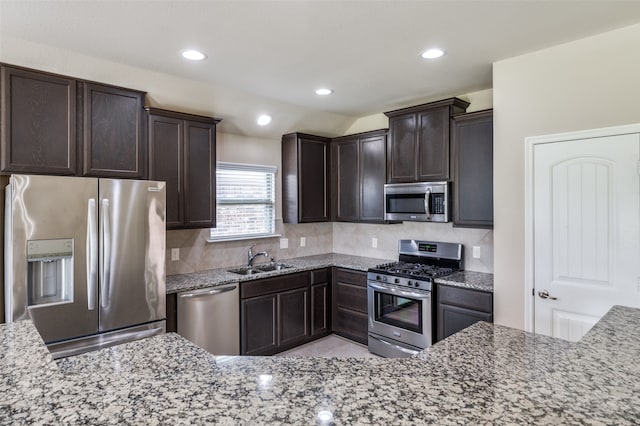 kitchen featuring sink, light stone counters, dark brown cabinets, appliances with stainless steel finishes, and decorative backsplash