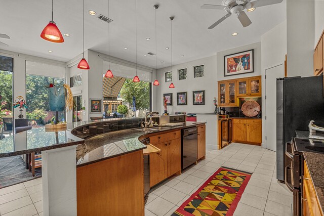 kitchen with pendant lighting, light tile patterned flooring, stainless steel range with electric stovetop, ceiling fan, and a large island with sink