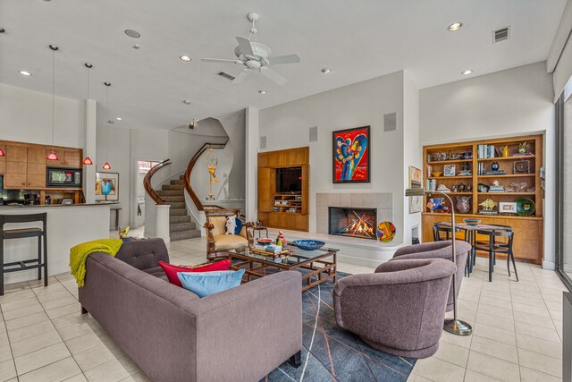 living room with a tile fireplace, ceiling fan, light tile patterned flooring, and a towering ceiling