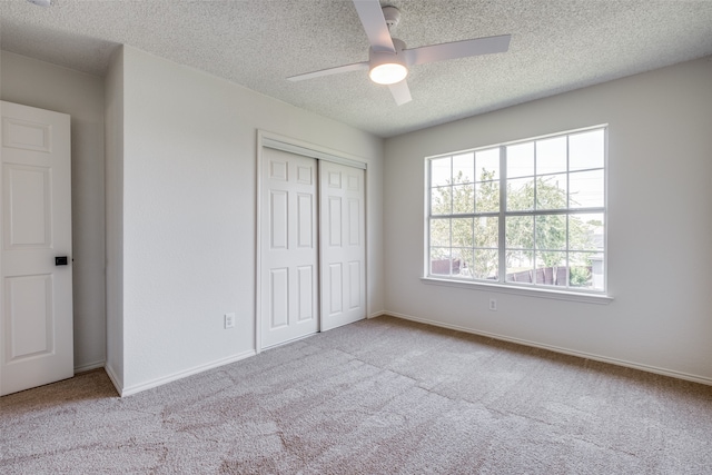 unfurnished bedroom featuring multiple windows, a textured ceiling, light colored carpet, and ceiling fan