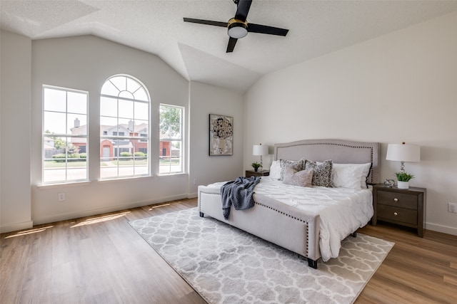 bedroom featuring wood-type flooring, vaulted ceiling, a textured ceiling, and ceiling fan