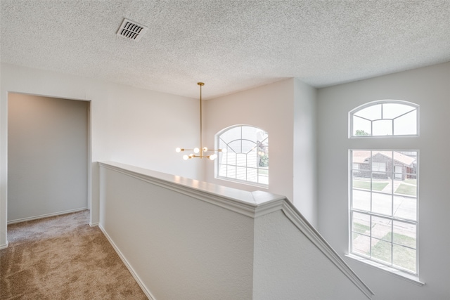 corridor with carpet flooring, a textured ceiling, and a chandelier