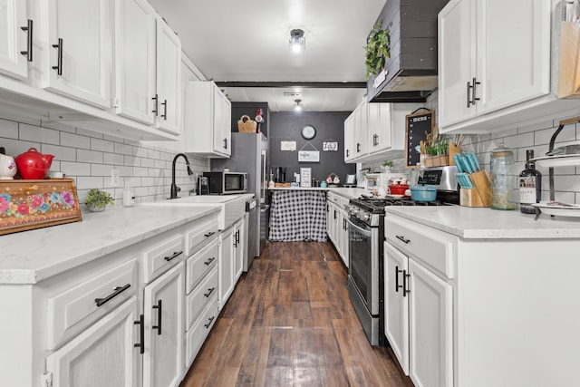 kitchen with appliances with stainless steel finishes, backsplash, white cabinetry, dark wood-type flooring, and wall chimney exhaust hood