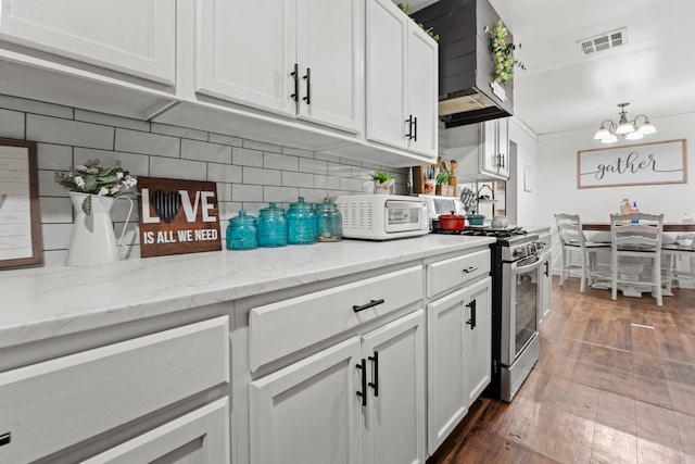 kitchen featuring stainless steel gas range oven, wall chimney range hood, white cabinets, backsplash, and hardwood / wood-style floors