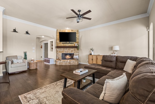 living room with ceiling fan, dark hardwood / wood-style flooring, a stone fireplace, and crown molding