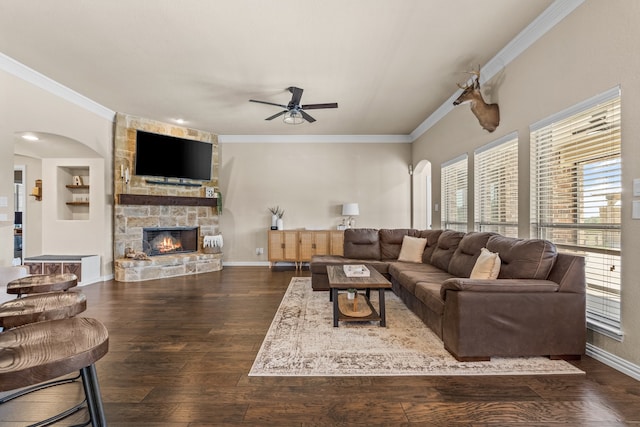 living room with built in features, a stone fireplace, dark hardwood / wood-style flooring, ceiling fan, and ornamental molding