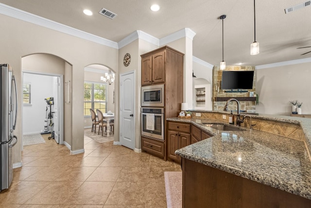 kitchen featuring sink, appliances with stainless steel finishes, hanging light fixtures, ornamental molding, and dark stone counters