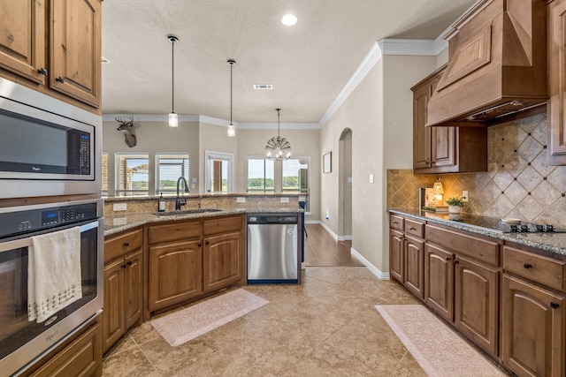 kitchen featuring premium range hood, sink, light stone counters, decorative light fixtures, and appliances with stainless steel finishes