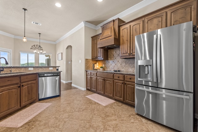 kitchen featuring crown molding, custom exhaust hood, appliances with stainless steel finishes, decorative light fixtures, and sink