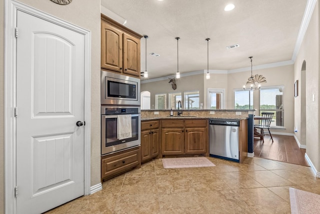 kitchen with pendant lighting, sink, crown molding, appliances with stainless steel finishes, and light stone countertops