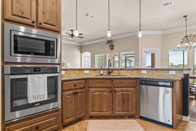 kitchen featuring appliances with stainless steel finishes, pendant lighting, sink, light stone counters, and crown molding