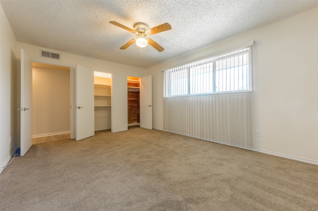 unfurnished bedroom featuring a textured ceiling, light colored carpet, a walk in closet, and ceiling fan