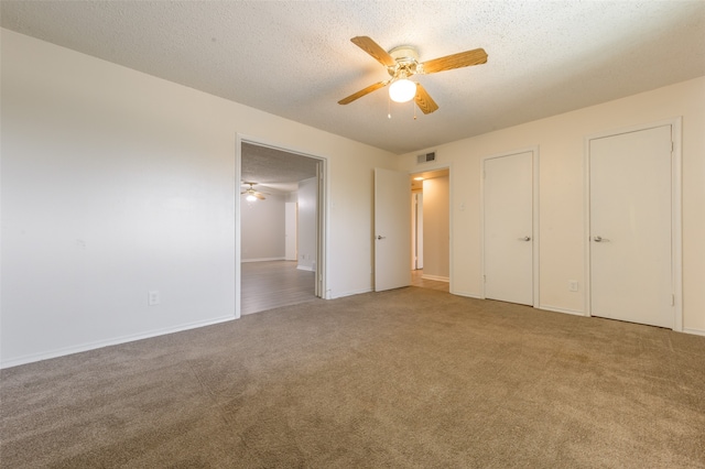 unfurnished bedroom featuring two closets, carpet, ceiling fan, and a textured ceiling