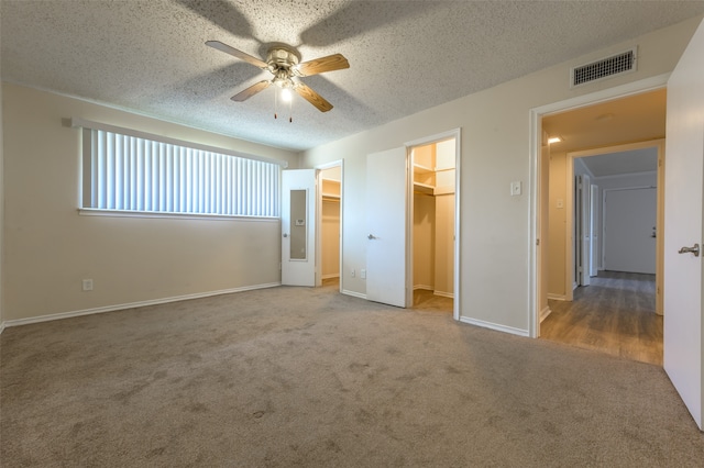 unfurnished bedroom with a textured ceiling, ceiling fan, light colored carpet, a walk in closet, and a closet