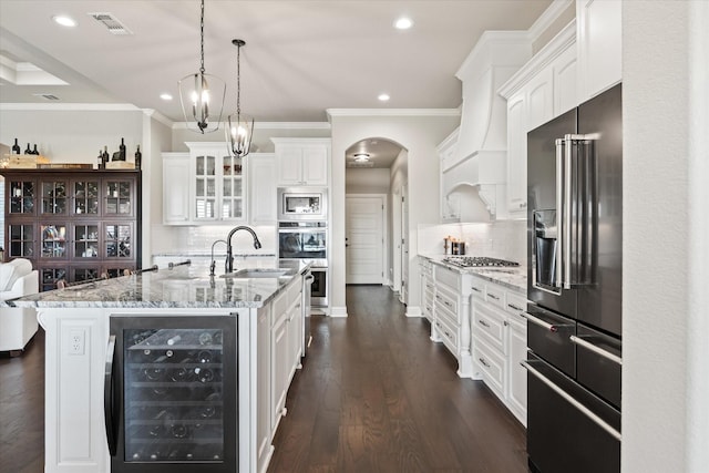 kitchen with appliances with stainless steel finishes, beverage cooler, a kitchen island with sink, and white cabinets