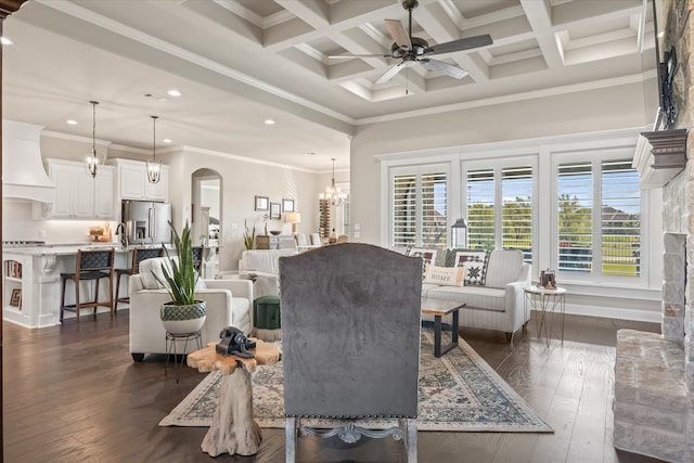 living room featuring dark wood-type flooring, beamed ceiling, ceiling fan with notable chandelier, and coffered ceiling