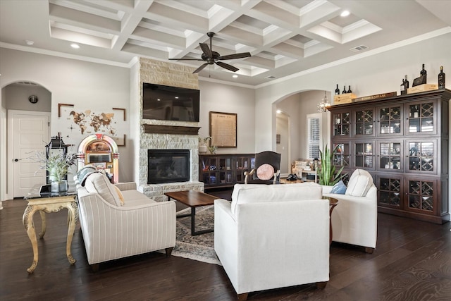 living room featuring a stone fireplace, dark hardwood / wood-style flooring, coffered ceiling, ceiling fan, and beam ceiling